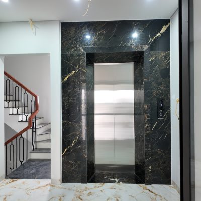Lift landing door with a metal finish and dark stone surround at a Tan Long project
